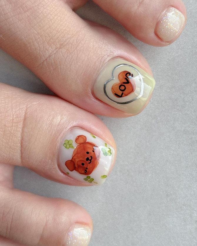 Toe nails with hand-painted teddy bear, green clovers, and double heart with “Love” text on a nude base