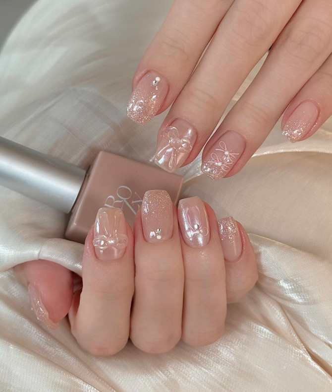 Blush pink nails with glitter, 3D bows, and pearls.