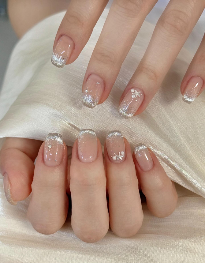 Nude nails with silver glitter French tips and pearl charms.
