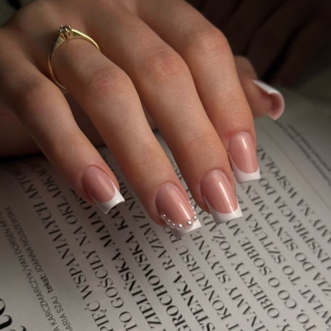 Square French tip bridal nails with a glossy nude base and delicate pearl details—perfect for a classic and luxurious wedding look. Classic French bridal nails with subtle sparkle