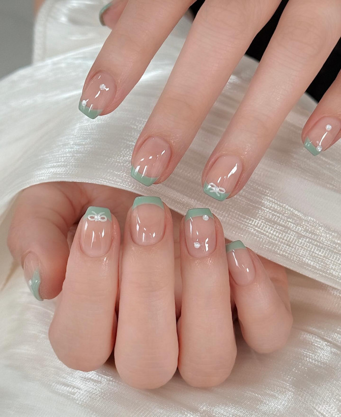 Mint green French tips with mini white bows on a nude base.