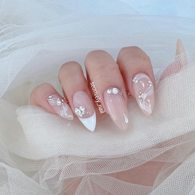 Nude almond bridal nails with white French tips, delicate floral line art, and crystal embellishments—ideal for an ethereal and romantic wedding manicure.3D floral bridal nail art for weddings