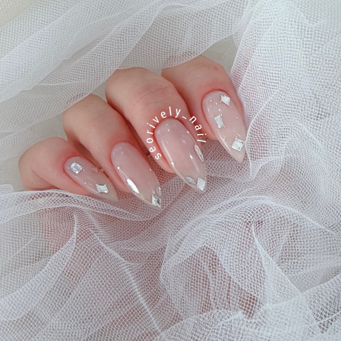 Glossy nude almond nails with silver foil tips and square crystal embellishments—perfect for a chic, contemporary bridal look.
