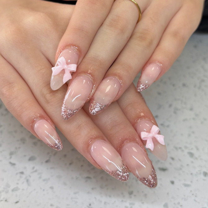 Glossy almond bridal nails with pink glitter French tips and 3D pastel pink bows, perfect for a sweet and glamorous wedding day look.
