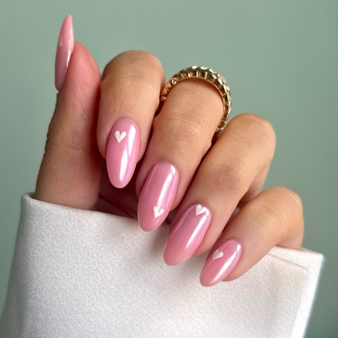 Glossy soft pink almond-shaped nails with delicate white heart details, offering a sweet and romantic bridal manicure.
