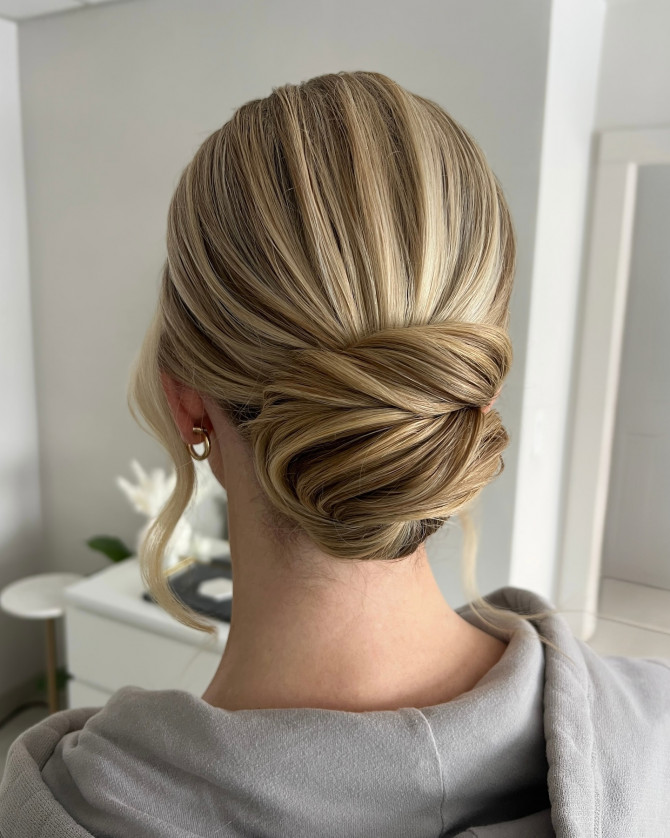 Sleek folded bridal low bun with blonde highlights and soft framing pieces by @erikataftbridal