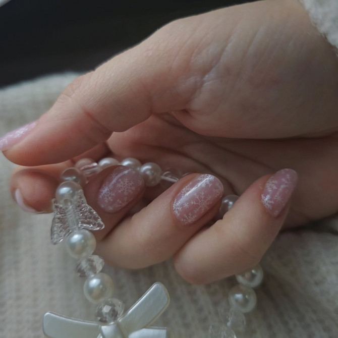 Soft pink bridal nails with delicate white snowflake patterns over a sheer base, creating a dreamy and whimsical winter wedding look.