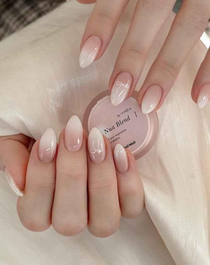 Gradient nude-to-pink nails with hand-painted white bow.