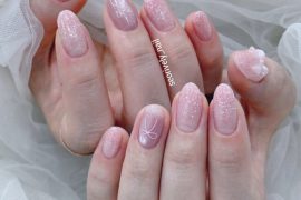 Glittery pink bridal nails featuring soft ombré shimmer, delicate ribbon line art, and 3D bow embellishments—perfect for a sweet and whimsical wedding style.