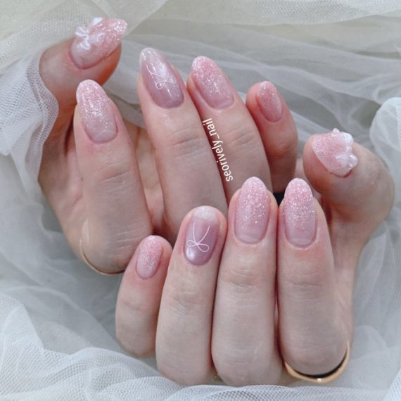 Glittery pink bridal nails featuring soft ombré shimmer, delicate ribbon line art, and 3D bow embellishments—perfect for a sweet and whimsical wedding style.