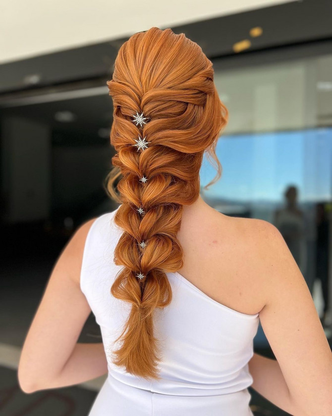 Long red bridal hair styled in a voluminous pull-through braid with star-shaped pins by @penteadoslucena. Romantic bridal hairstyle with caramel curls and twisted crown