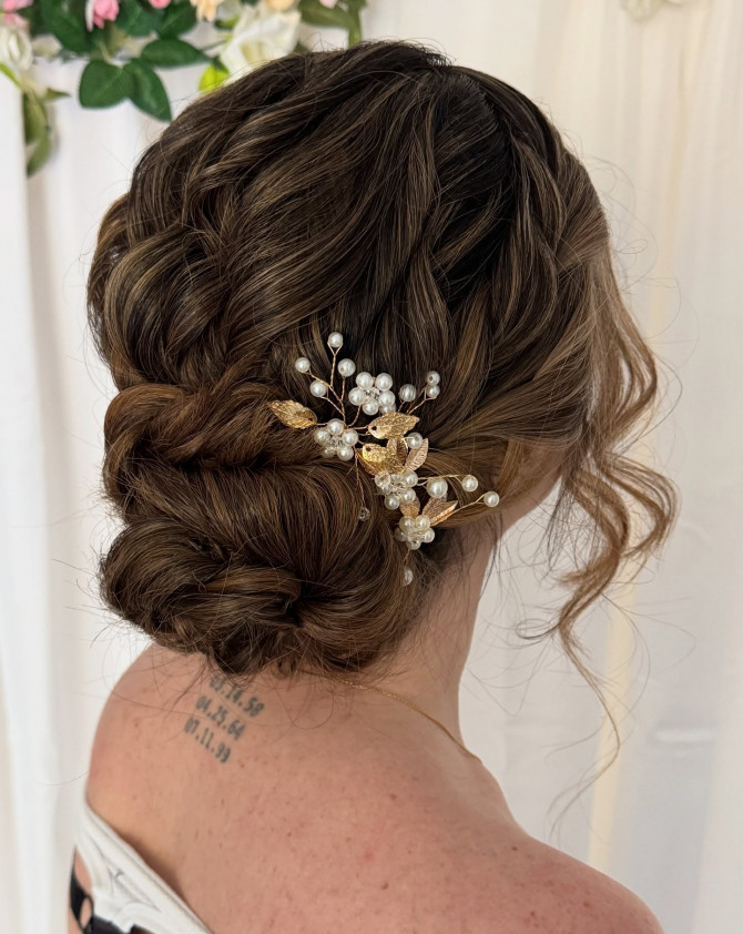 Low braided bridal bun with gold and pearl comb, soft face-framing tendrils.