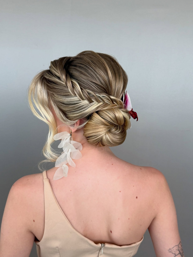 Side-twist low bun with fishtail detail and orchid pin.