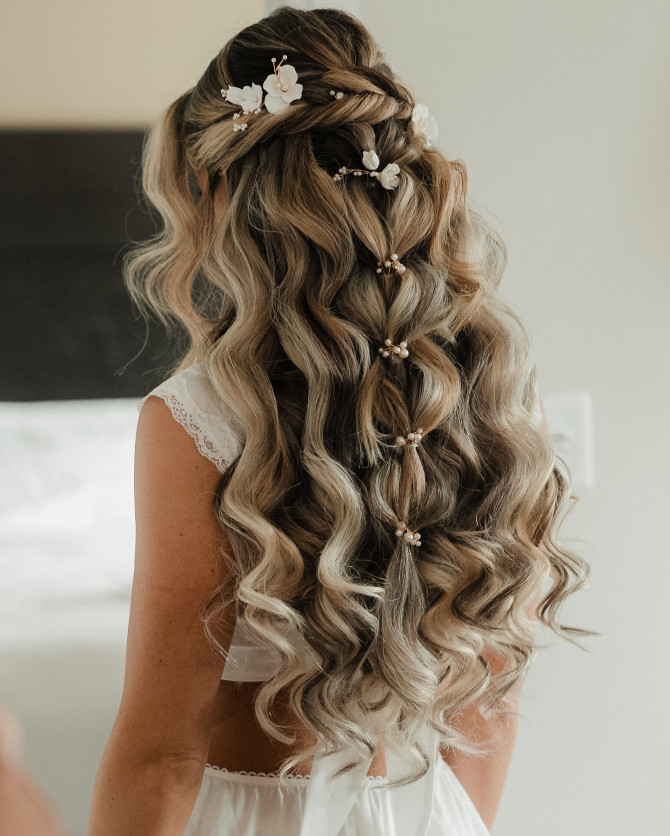 Half-up bridal hairstyle with long curls, pearl accents, and white flower hair clips
