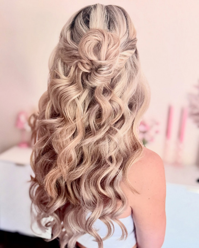 Half-up bridal hairstyle with rose bun and soft voluminous curls