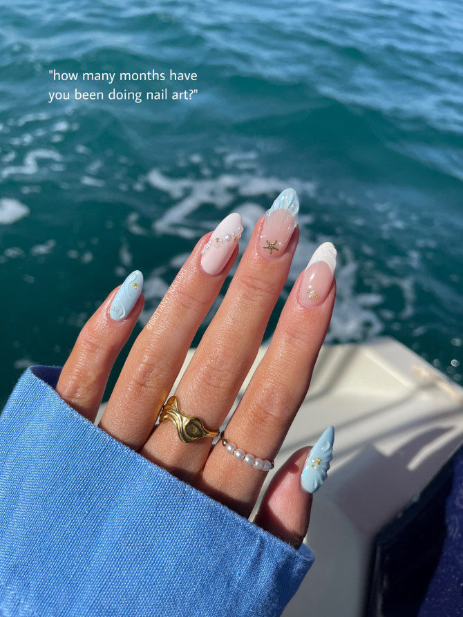 Ocean-inspired acrylic nails with blue waves, pearls, and starfish decals