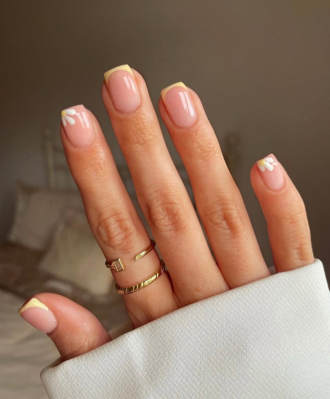 Minimal nude acrylic nails with yellow French tips and daisy accent