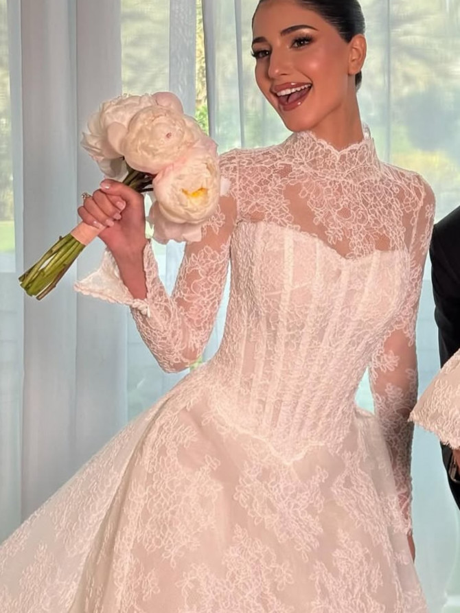 High-neck lace bridal gown with corseted bodice and long sleeves; joyful bride holding peonies.