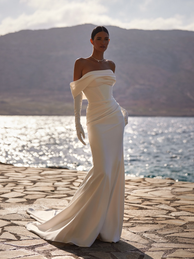 Off-shoulder corseted column with gloves by the water; refined bridal gowns silhouette. 