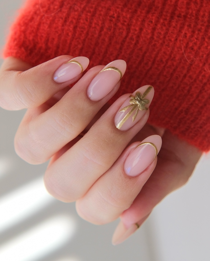 Soft pink almond nails with gold French tips and ribbon bow accent for festive bridal looks